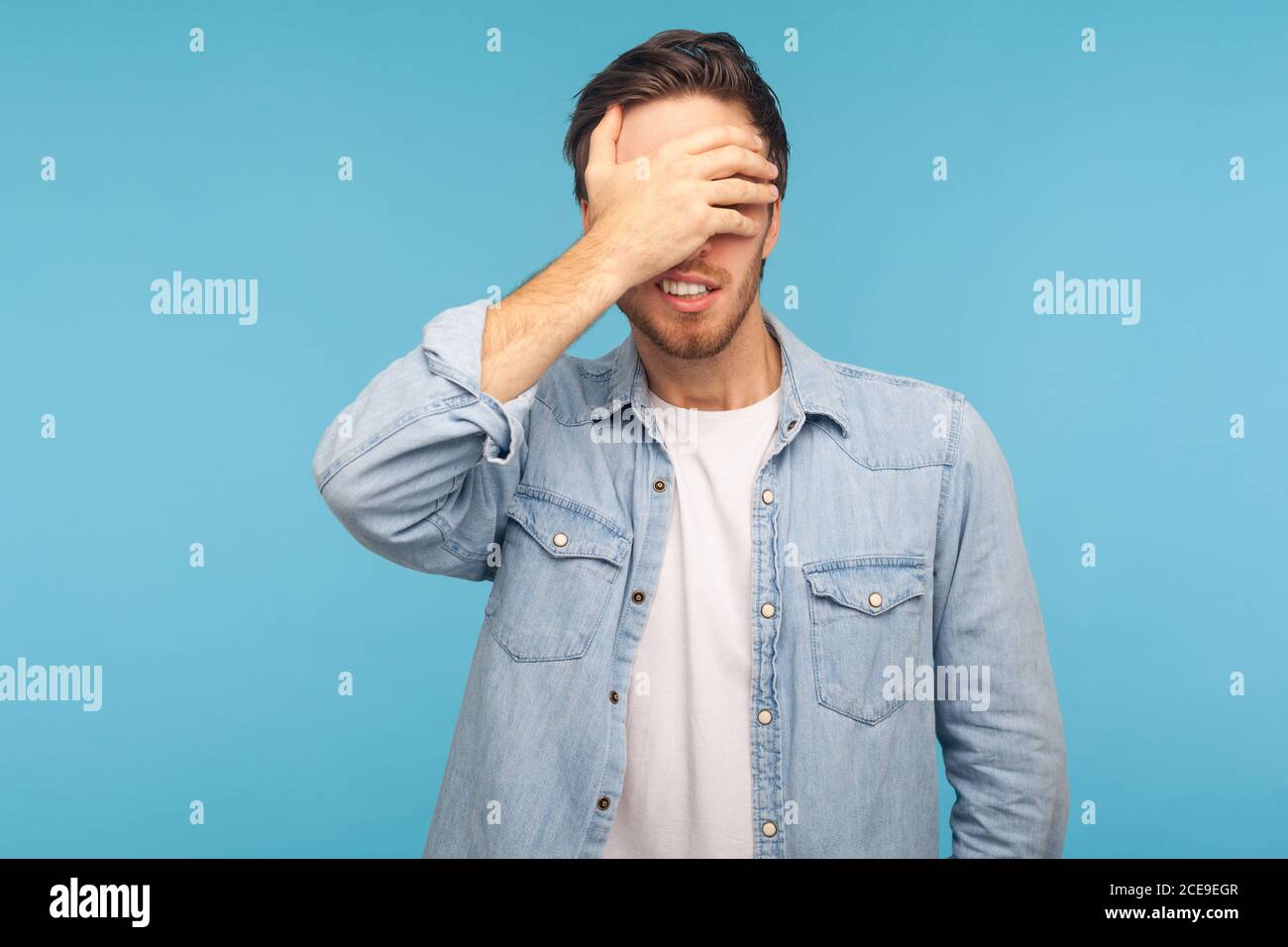 Don't want to watch! Portrait of confused shy man in worker denim shirt covering eyes, refusing to look at shameful content, scared afraid to see. ind Stock Photo