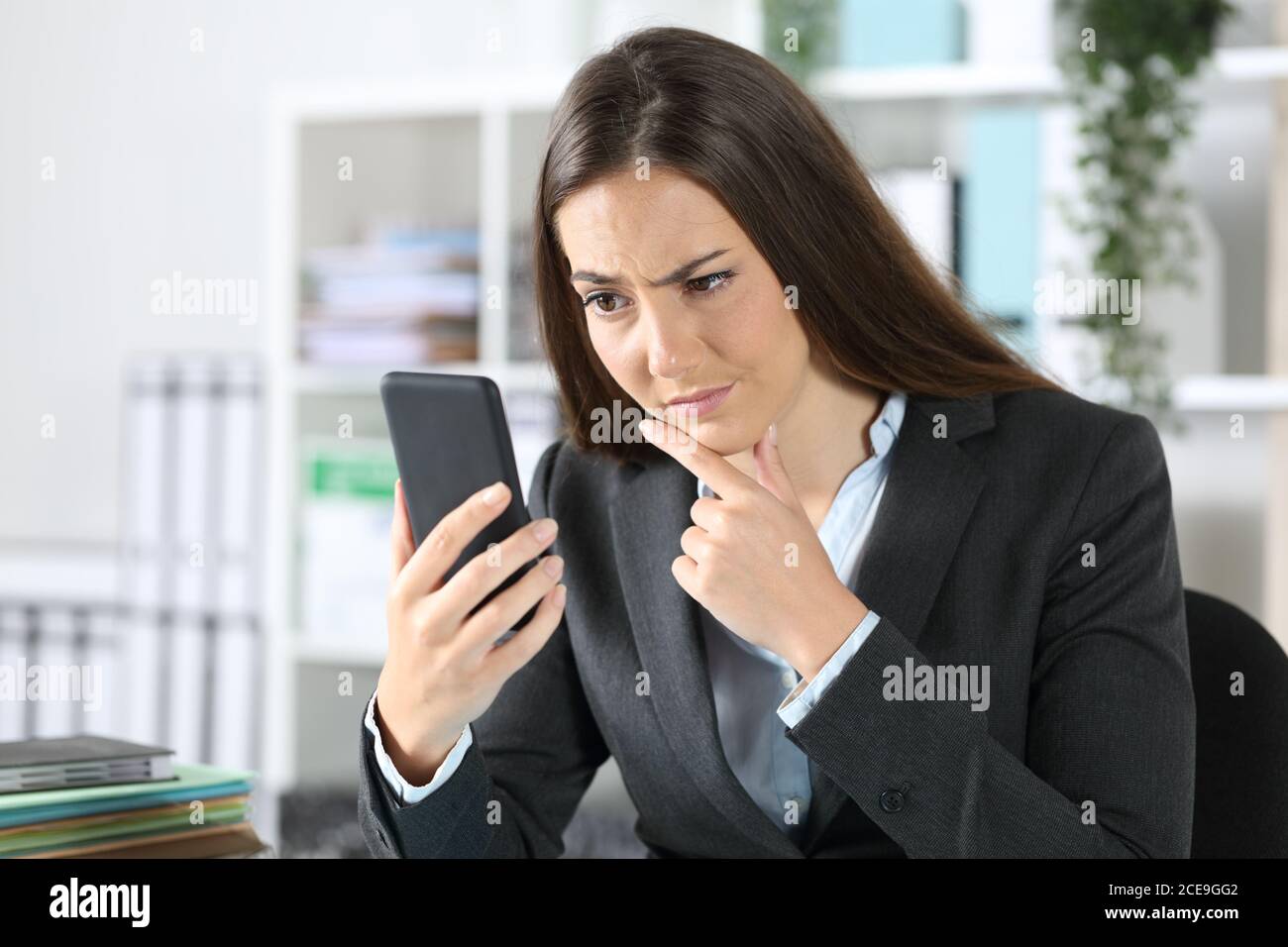 Suspicious executive woman checking smart phone sitting on a desk at the office Stock Photo