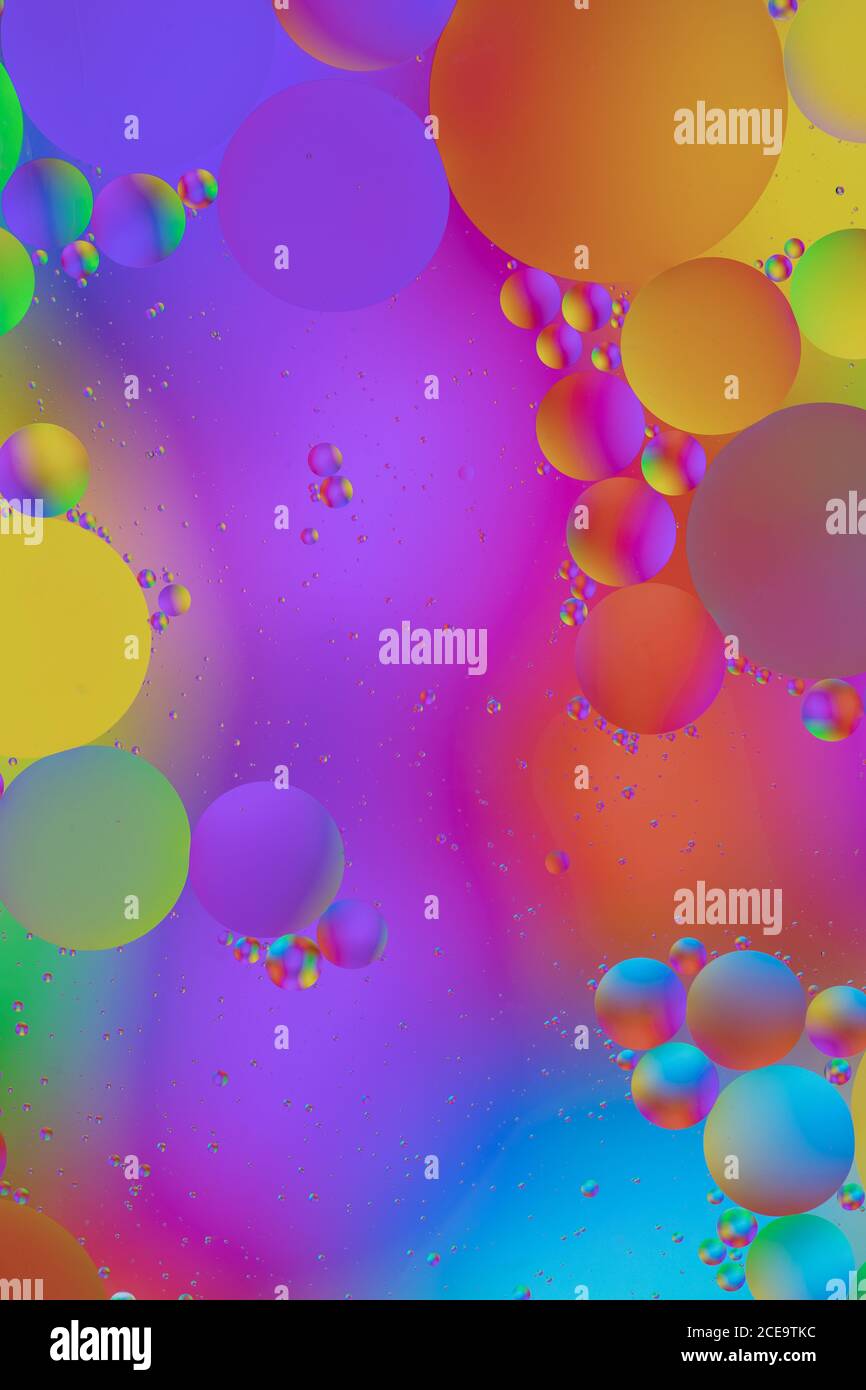 Macro photo of mixing oil and water. Oil droplets above a beautiful coloured abstract background creating circles and ovals. Stock Photo