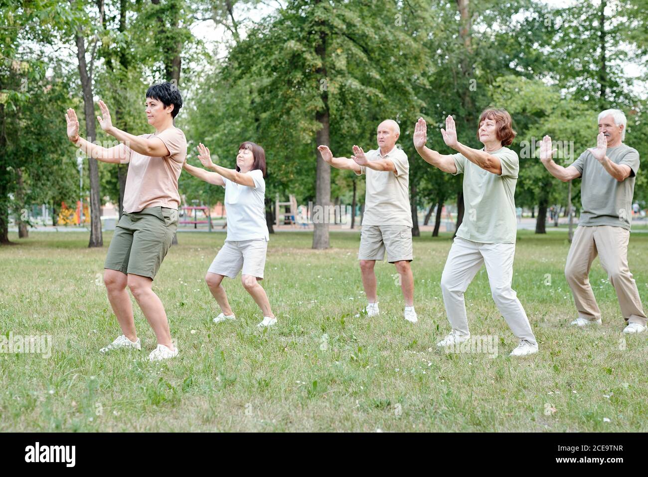 Focused coach raising hands forward while showing relaxing exercise to senior students at qigong practice Stock Photo