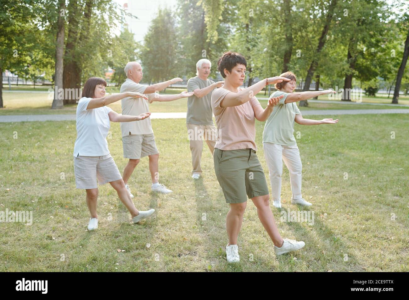 Group of focused senior people and their coach gesturing hands and doing qigong exercise in park Stock Photo