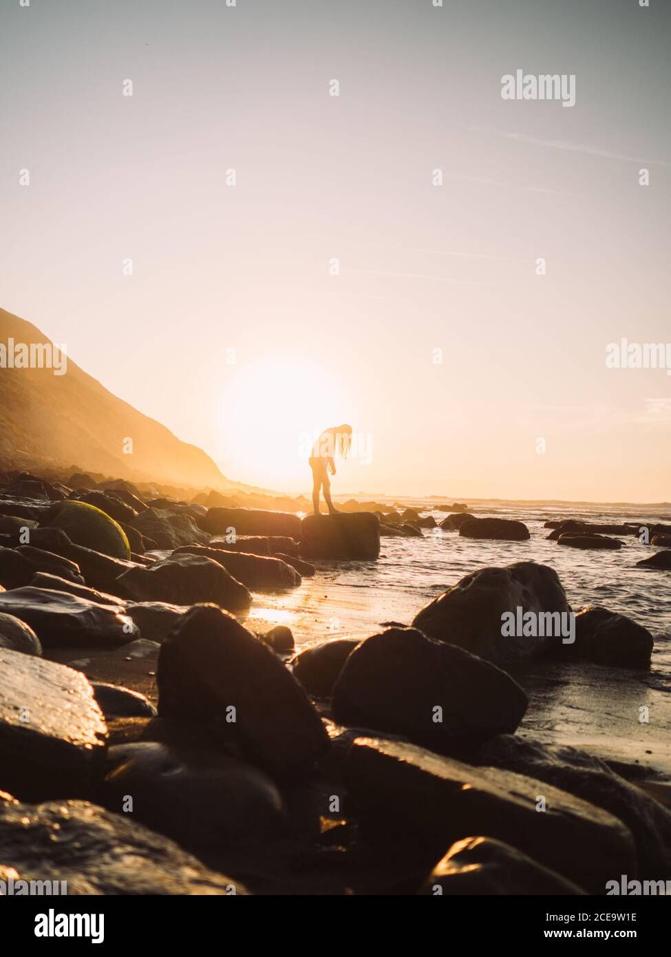 Female silhouette, standing on beach, with huge boulders coming out of sand, close up. Backlit. Stock Photo