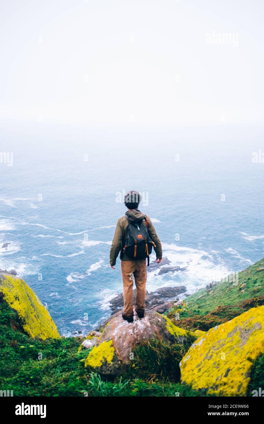 Lonely man standing on boulder and looking at beautiful seascape. High precipice. Epic view. Stock Photo