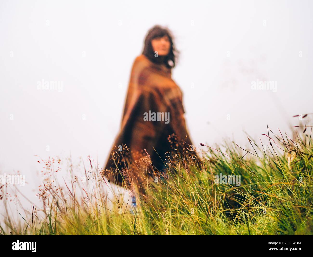 unrecognizable Woman in traditional scottish overcoat on sky background. Focus on green grass. Highlands, Scotland.OLYMPUS DIGITAL CAMERA Stock Photo