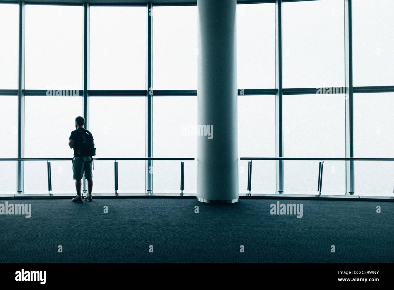 Back view of a person looking out of a window in modern building. Horizontal indoors shot. Stock Photo