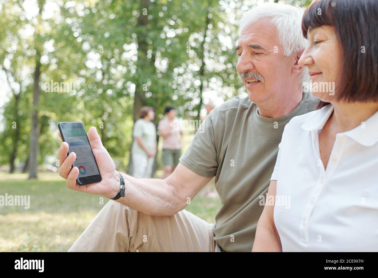 Modern senior man with mustache analyzing day activity with wife using mobile app in park Stock Photo