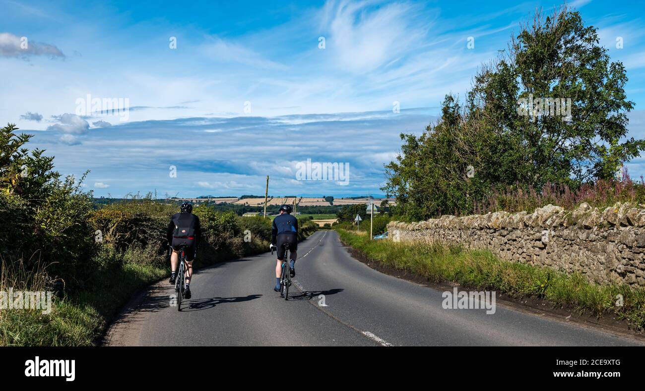 Two male cyclists on empty quiet country road on sunny Summer day, East Lothian, Scotland, UK Stock Photo