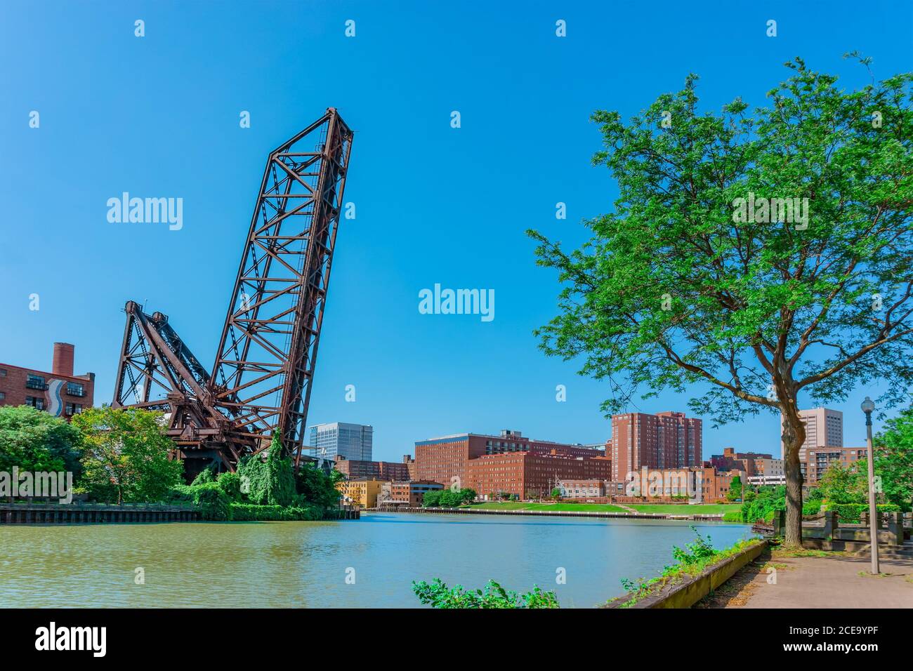 Cuyahoga River runs by a raised draw bridge and through the town of Cleveland, Ohio. Parks and brick buildings line both sides of the water. Stock Photo