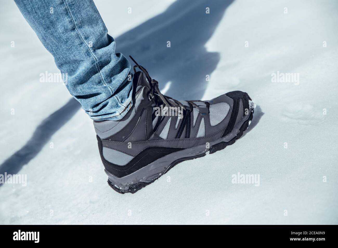 Side view of crop male leg in jeans and winter boot standing on snow in sunny day in Cerdanya, France Stock Photo