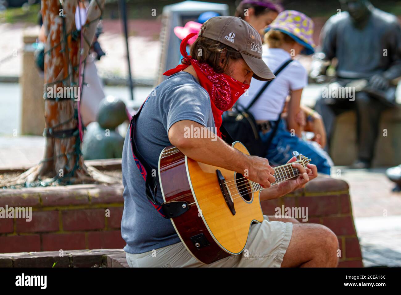 Annapolis, MD 08/21/2020: A young caucasian man is sitting on a brick wall in Annapolis marina and playing classical guitar. This street musician is w Stock Photo