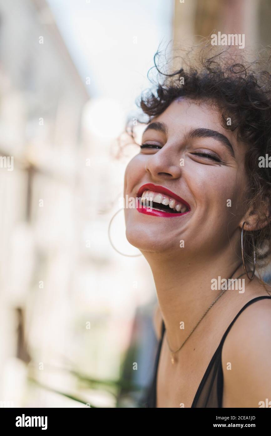 Close-up of charming curly girl in earrings and with red lips laughing happily and looking at camera Stock Photo