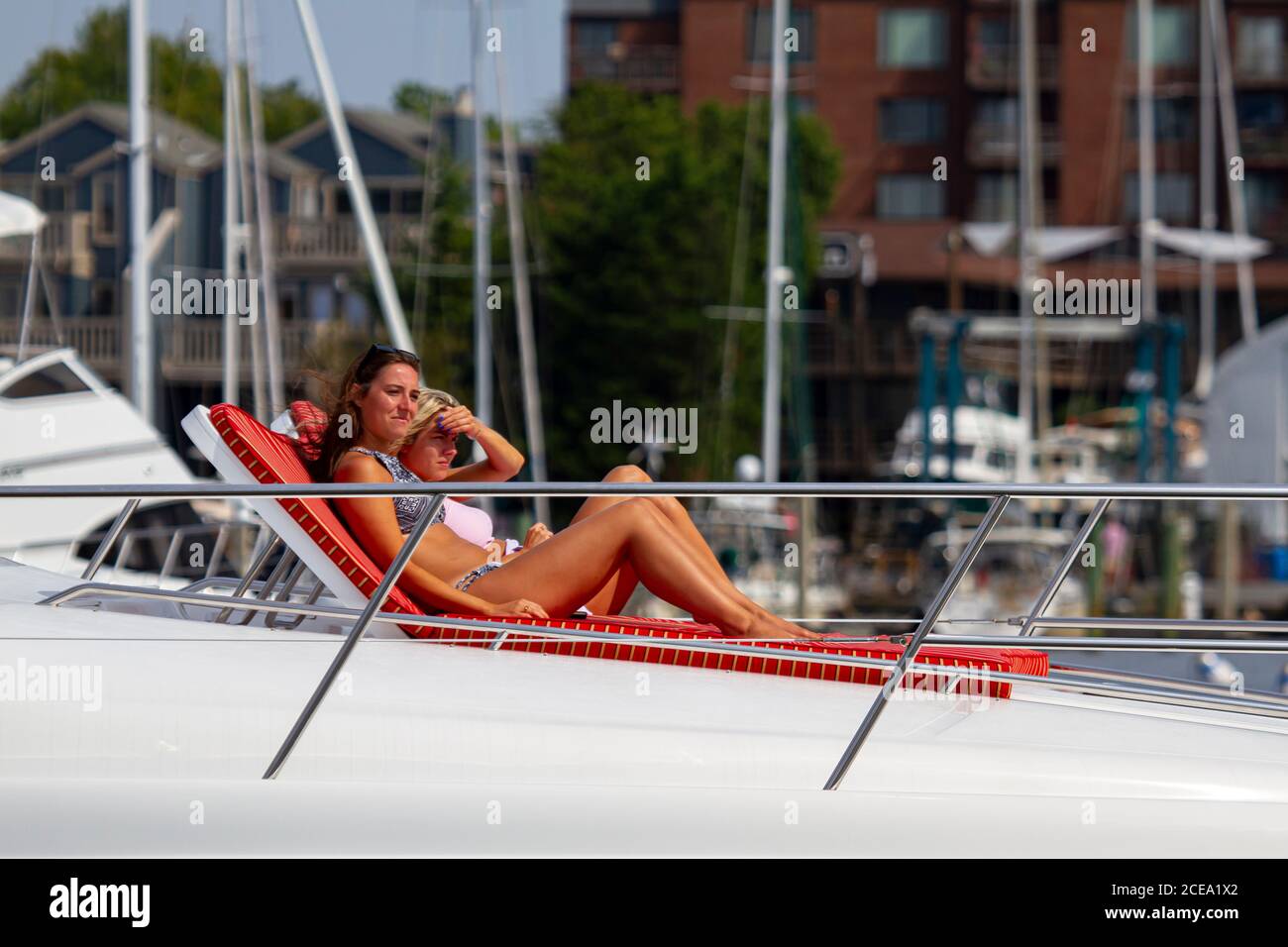 Annapolis, MD 08/21/2020: A blonde and a brunette woman are sunbathing on the deck of a yacht entering Annapolis marina. These young and beautiful wom Stock Photo