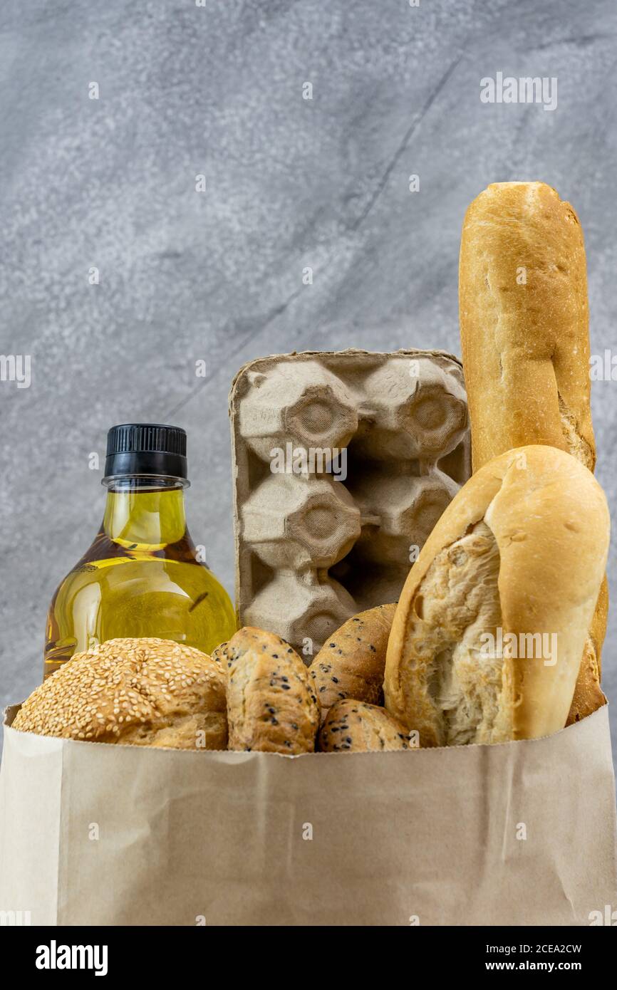 Grocery bag with egg cooking oil and variety of bread in disposable paper bag on grey vintage loft background. Bakery food and drink and grocery conce Stock Photo