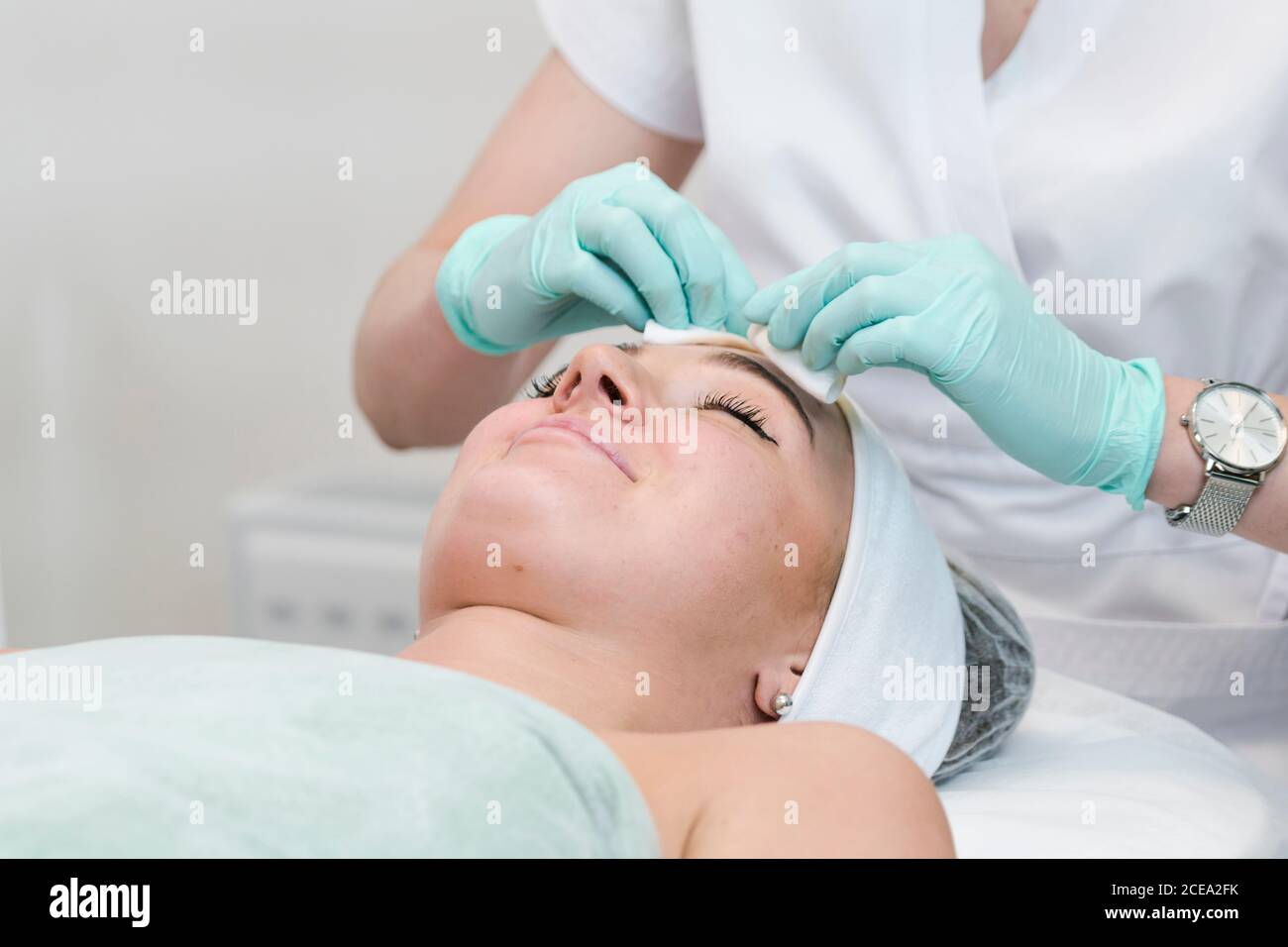 The young female client of cosmetic salon having a face cleaning procedure. The doctor cosmetologist cleaning skin with sponge. Concepts of skin care Stock Photo