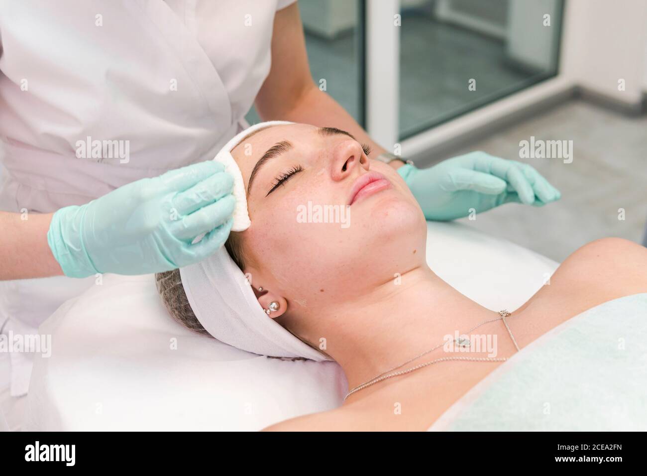 The young female client of cosmetic salon having a face cleaning procedure. The doctor cosmetologist cleaning skin with sponge. Concepts of skin care Stock Photo
