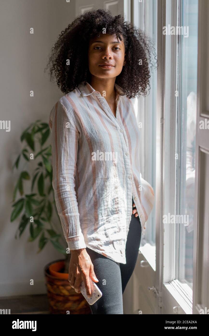 Young Woman standing at window and browsing smartphone Stock Photo