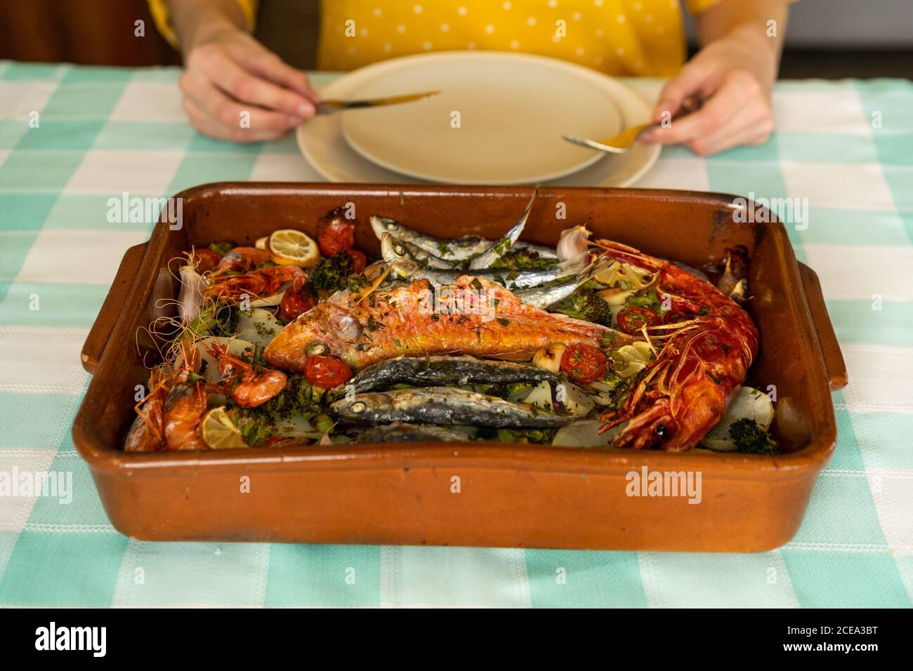 Hands of anonymous female using fork and knife to take delectable seafood dish from ceramic pan on table Stock Photo
