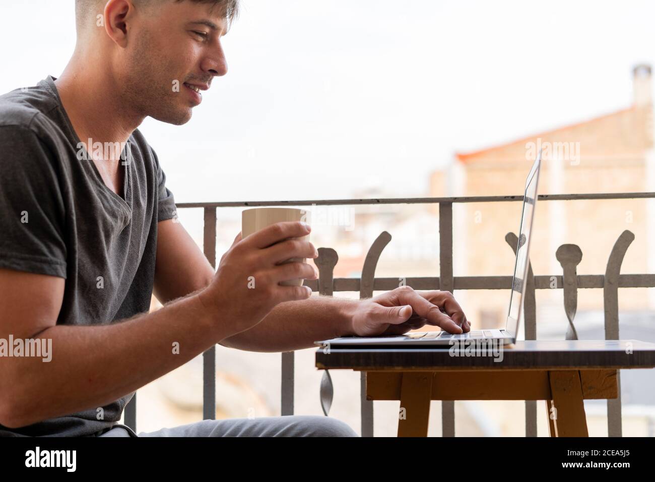 Handsome man with cup of coffee and using laptop on balcony Stock Photo