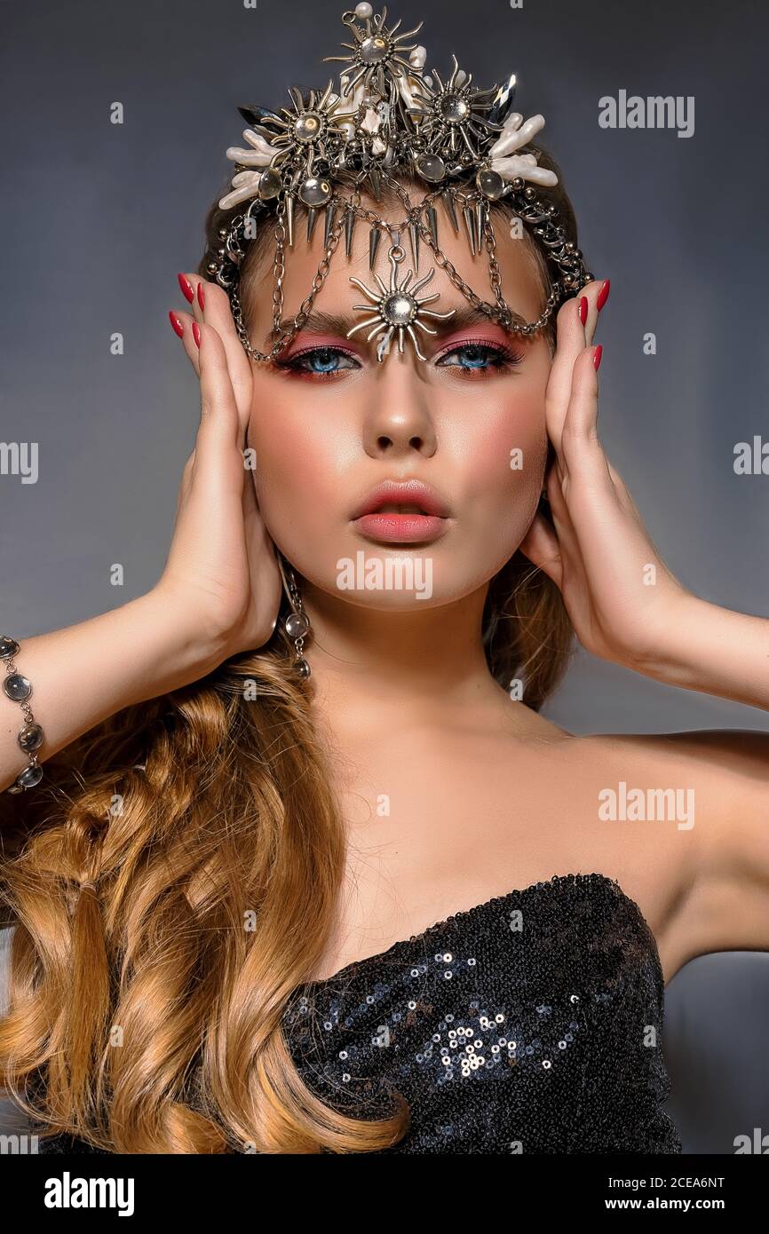 Close up portrait of a young beautiful blonde woman wearing a crown and costume jewelry on a gray background. Beauty concept Stock Photo