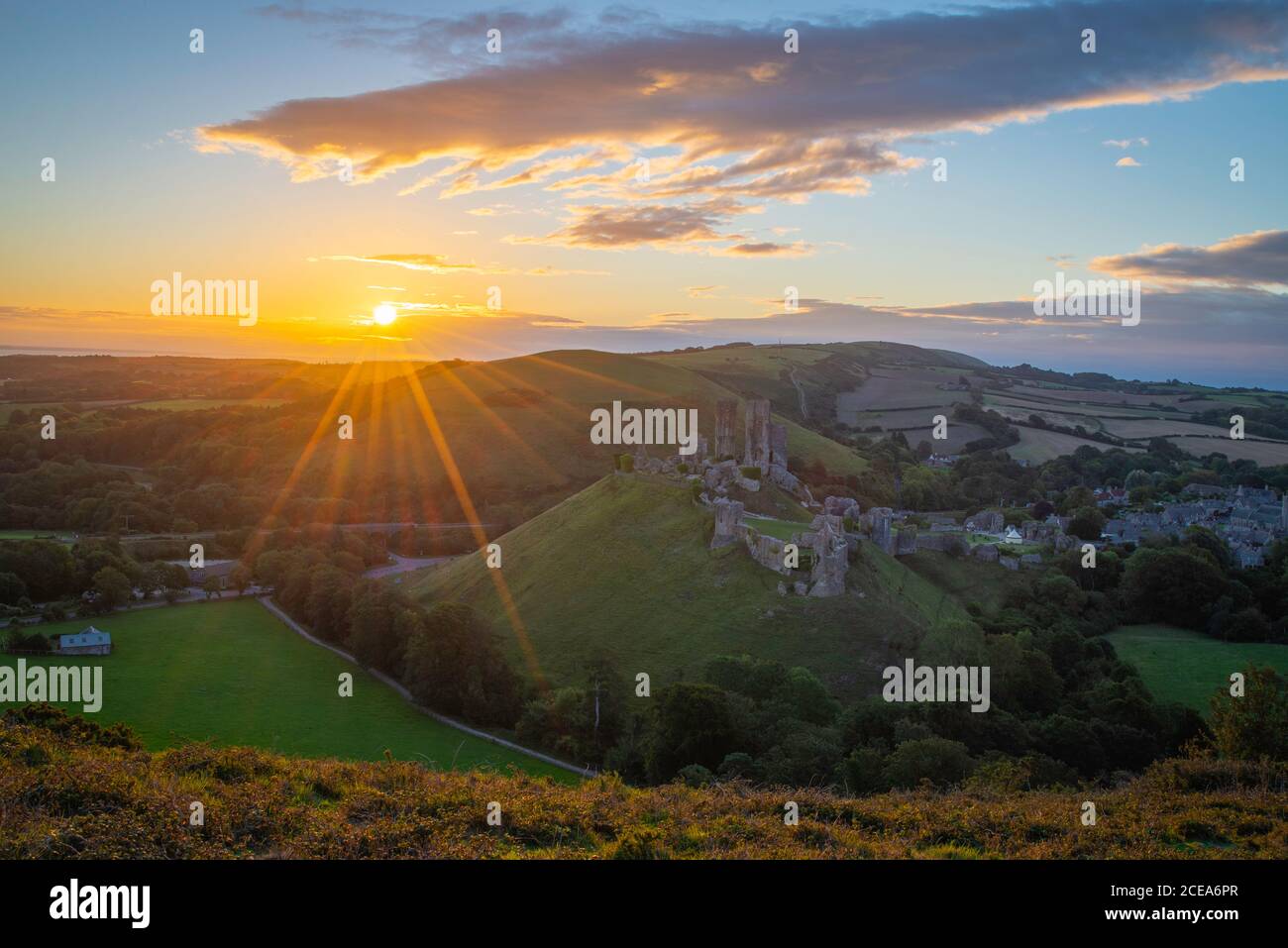 Sunrise with sunburst over the Dorset Countryside with Corfe castle and hills glowing from the morning sun. Stock Photo
