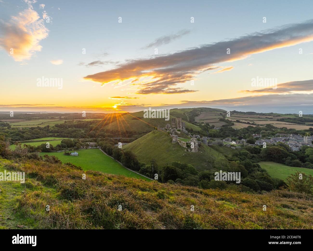 Sunrise with sunburst over the Dorset Countryside with Corfe castle and hills glowing from the morning sun. Stock Photo