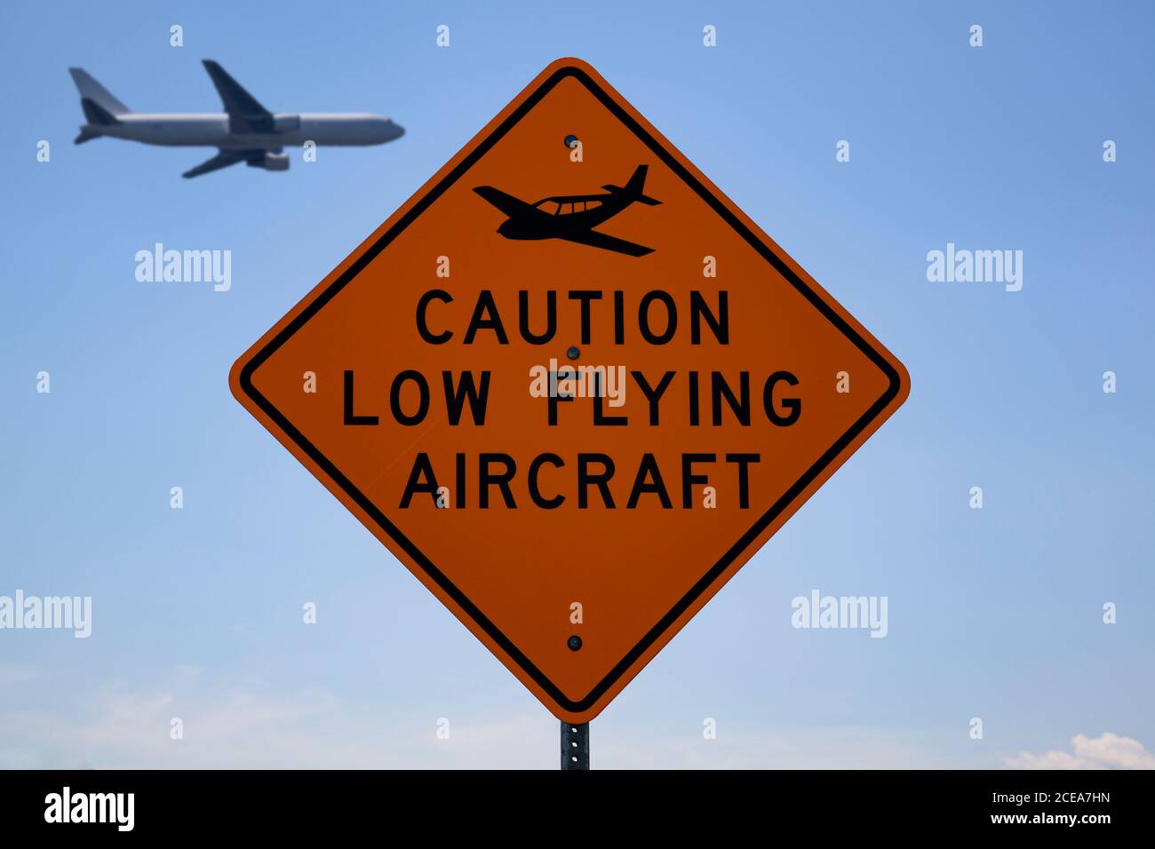 Stensville, MD 08/18/2020: Road sign near a local airfield which says 'Caution low flying aircraft' with a plane logo. A blurred passenger airplane is Stock Photo