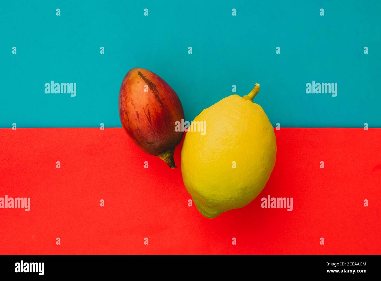 Fresh whole tamarillo and ripe lemon lying on bright red and blue background Stock Photo