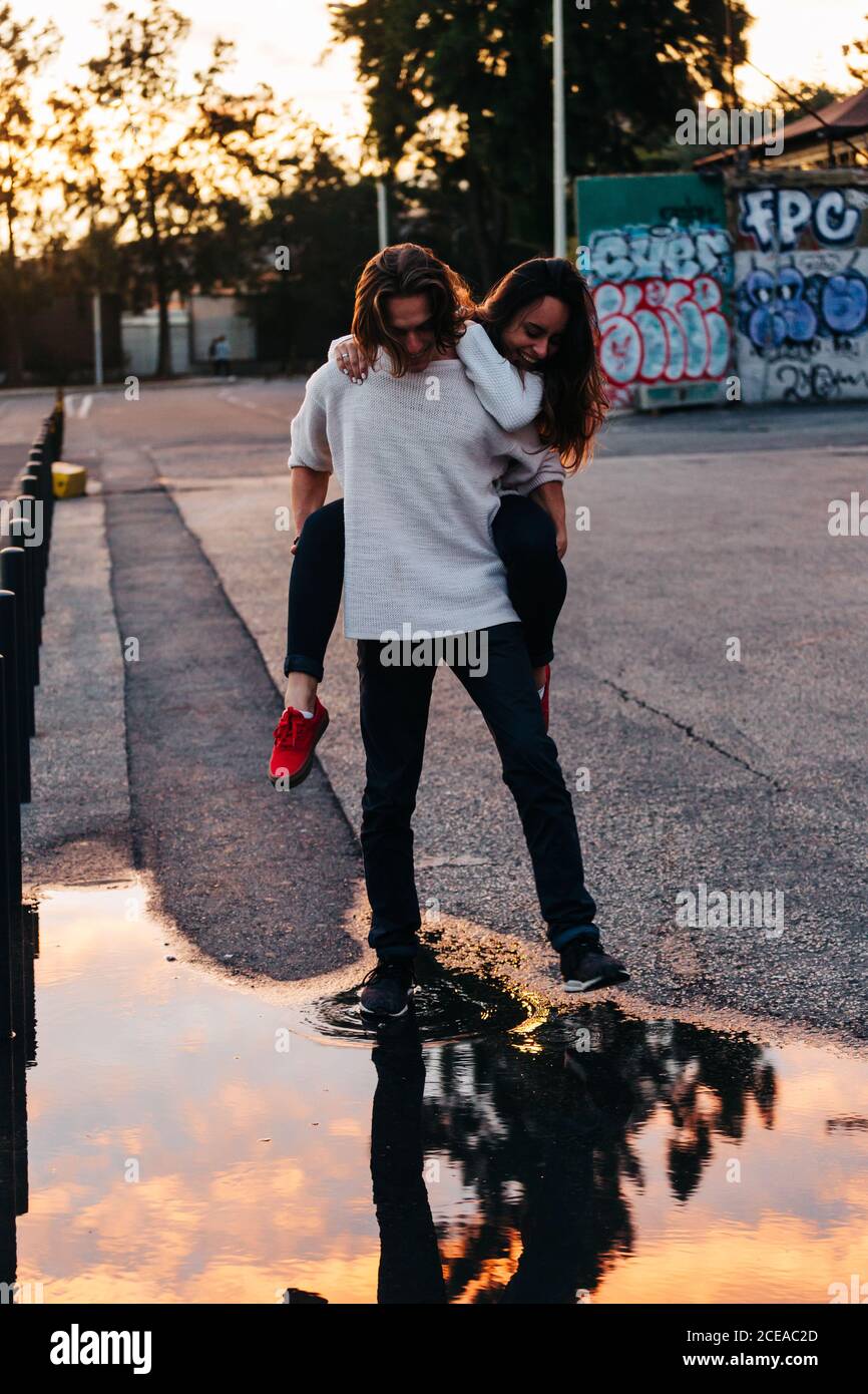 Reflection of young guy and lady in sweaters and jeans and beautiful sky in slop on street Stock Photo