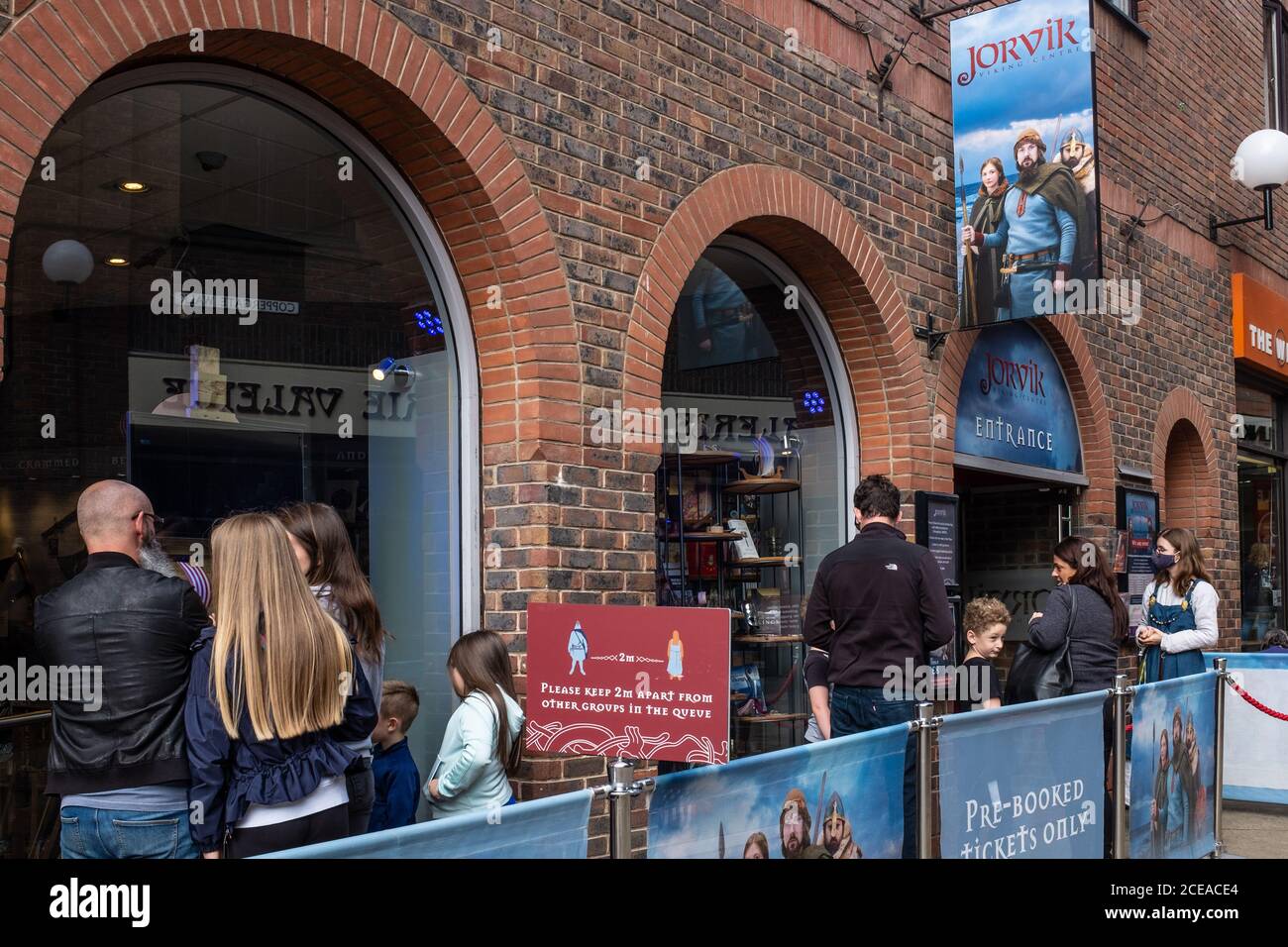 Queue of people with Pre booked tickets at Jorvik Viking Centre, York during coronavirus pandemic. With social distancing sign and staff wearing face Stock Photo
