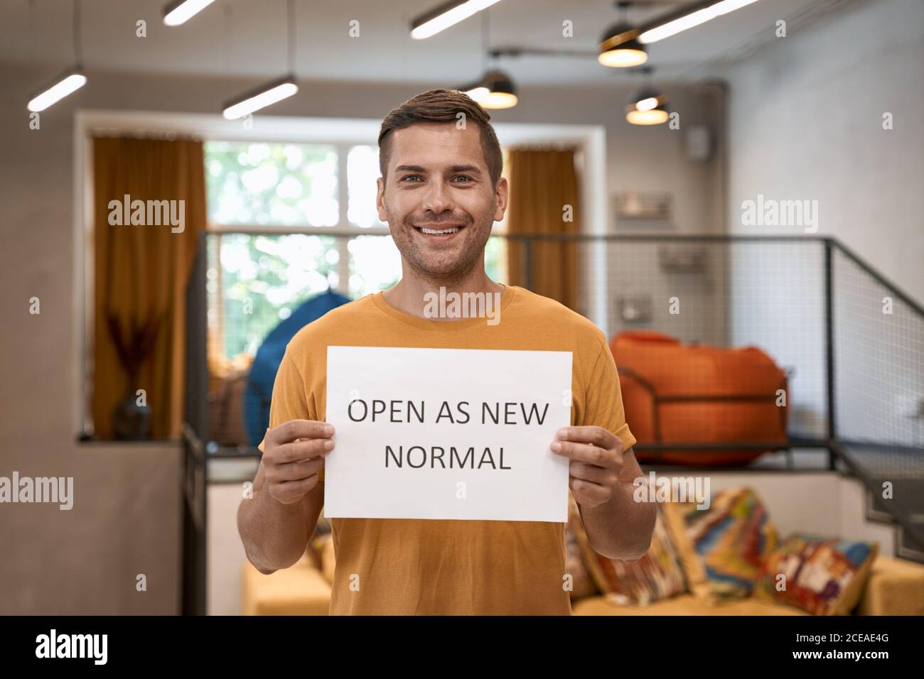 We are open. Young happy man, office worker showing paper with text OPEN AS NEW NORMAL and smiling at camera, standing in the modern coworking space Stock Photo