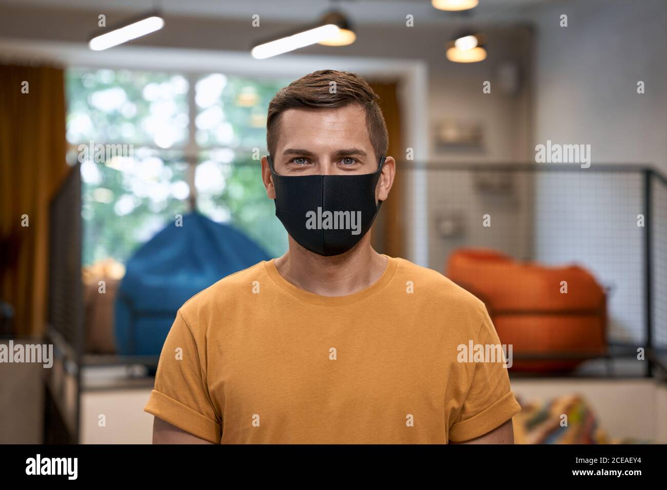 Working safely during coronavirus. Portrait of young man, male office worker wearing black protective mask and looking at camera, standing in the Stock Photo