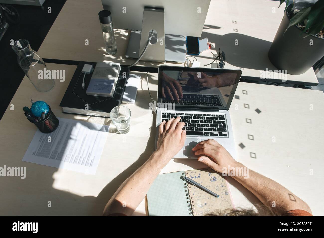 Crop shot from above of man sitting at table and working on laptop in bright sunlight inside of office Stock Photo