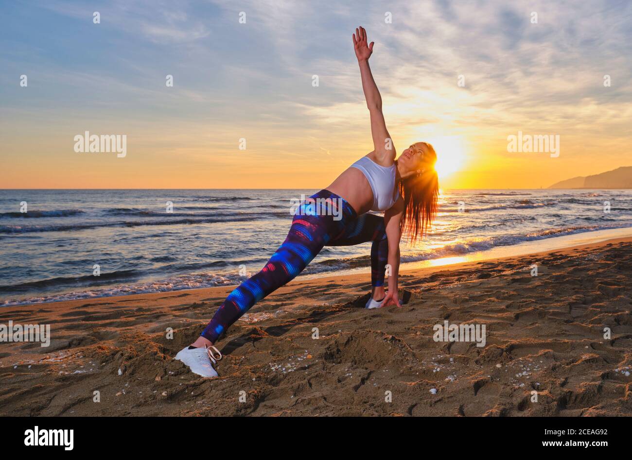 Attractive female in sportswear performing exercise and looking away while  standing on sandy coast near waving sea against cloudy sundown sky in  Castelldefels, Spain Stock Photo - Alamy