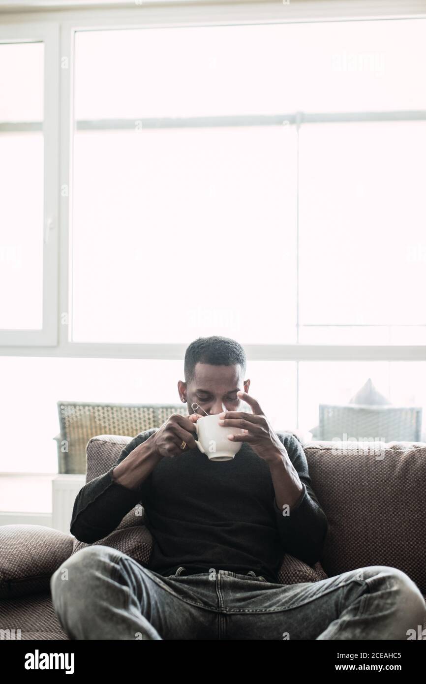 Pensive black man on sofa drinking coffee Stock Photo