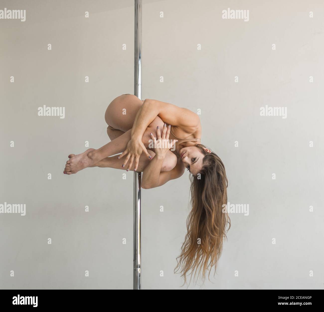 Young slim strong Woman practicing on pole in light room studio Stock Photo