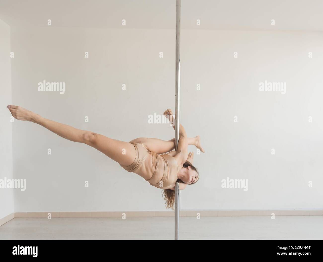 Young slim strong Woman practicing on pole in light room studio Stock Photo