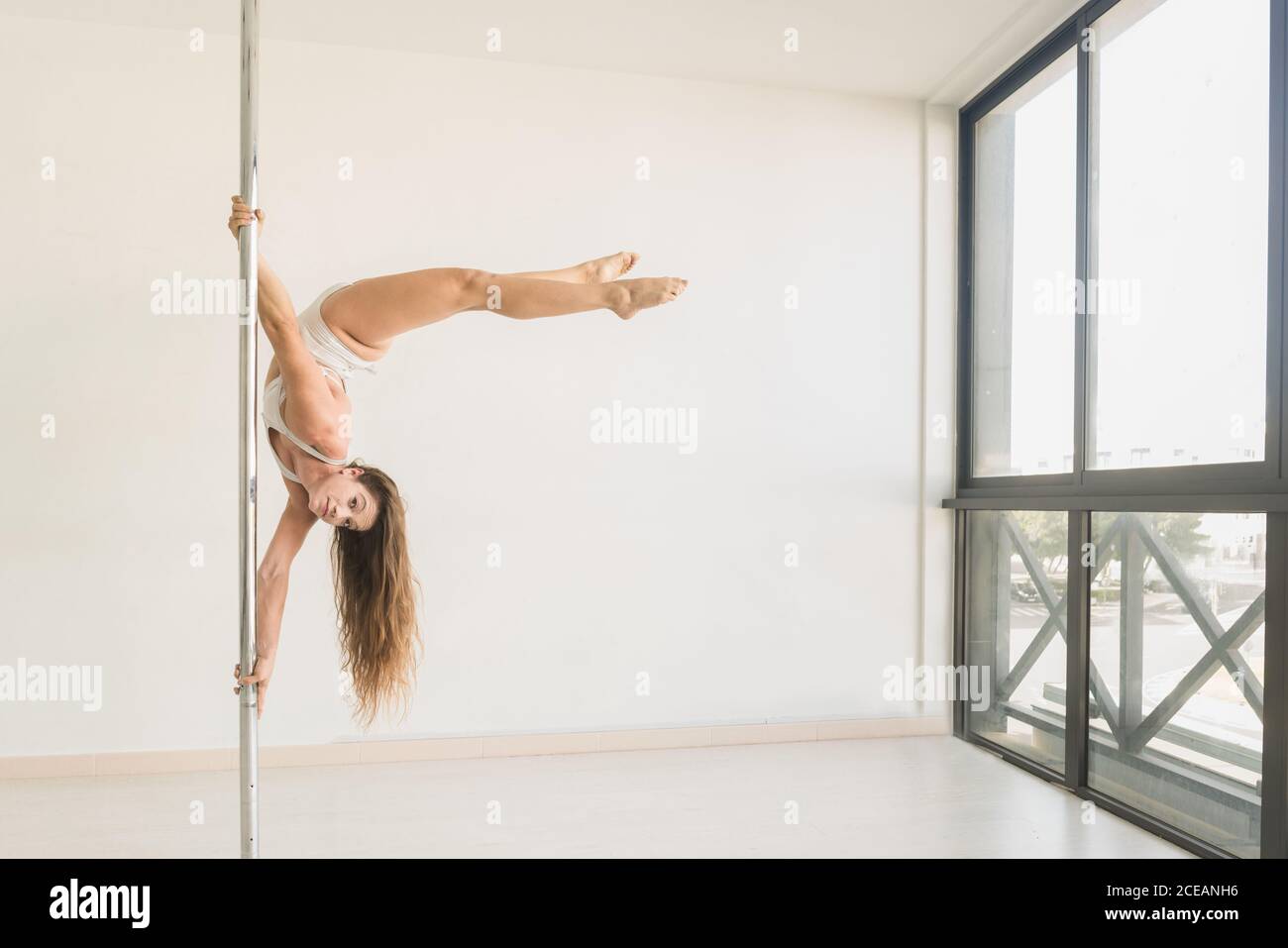 Young slim strong Woman practicing on pole in light room studio Stock Photo