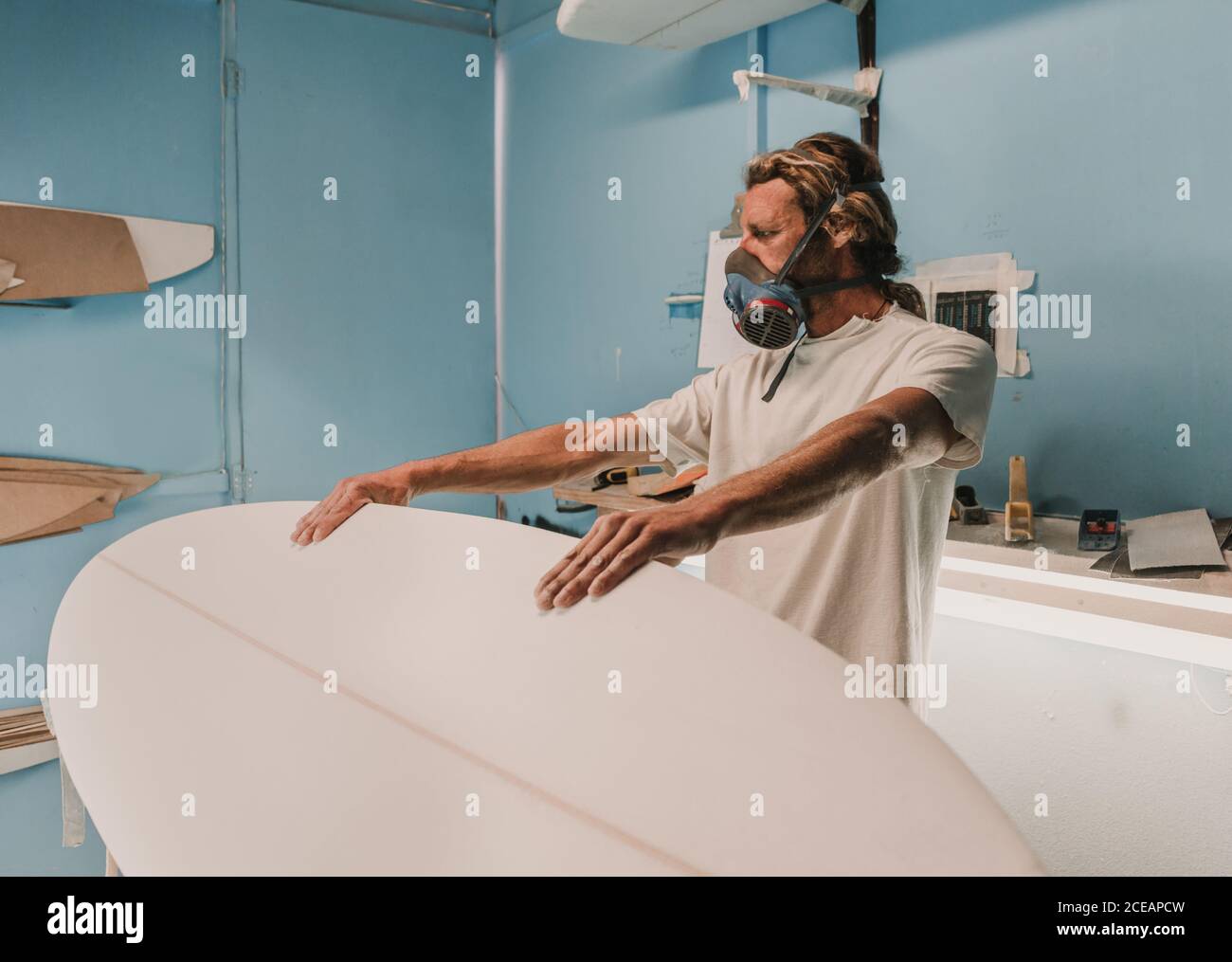man holding surf board on stand in workshop Stock Photo