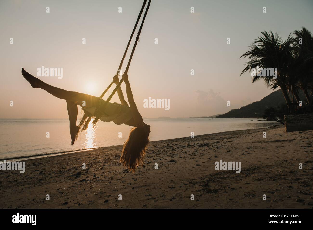 Side view of attractive Woman swinging on beach in sunset lights in