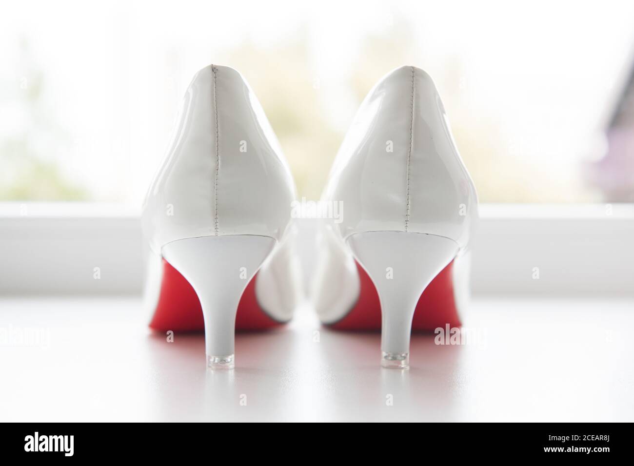 Beautiful classic white bridal shoes with red sole placed near window ...