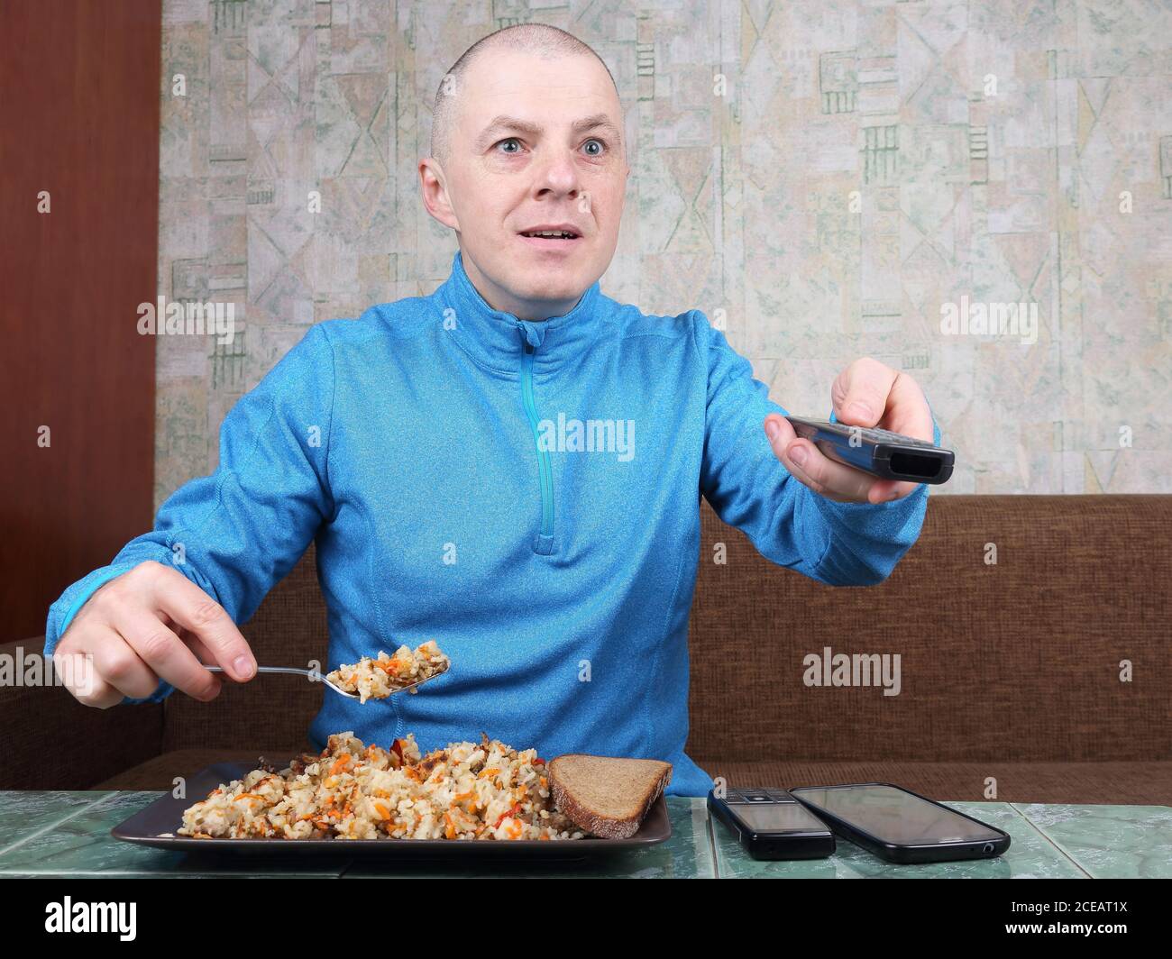the man eats rice pilaf and stares of TV program Stock Photo - Alamy