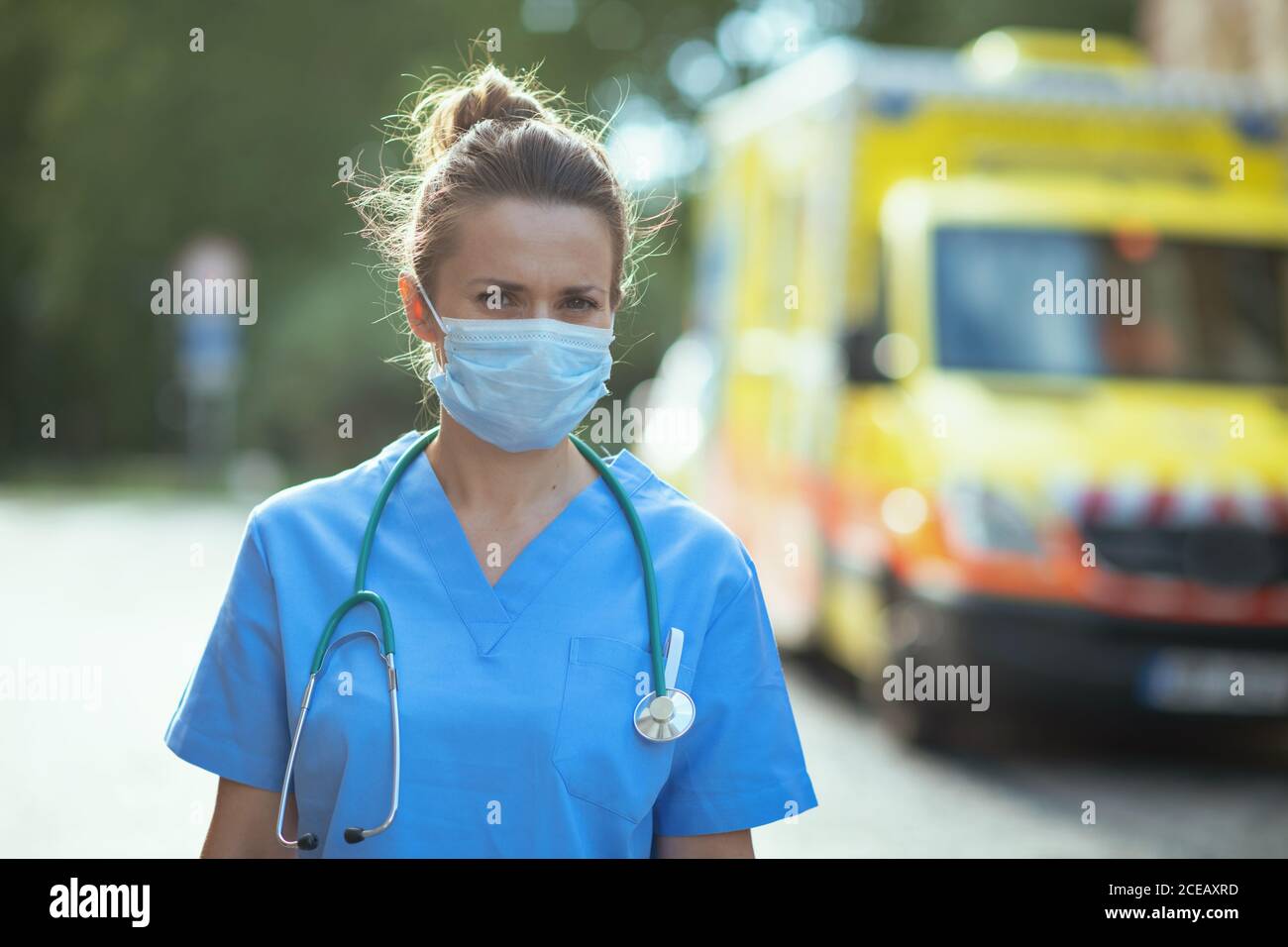 coronavirus pandemic. Portrait of modern medical doctor woman in uniform with stethoscope and medical mask outside near ambulance. Stock Photo