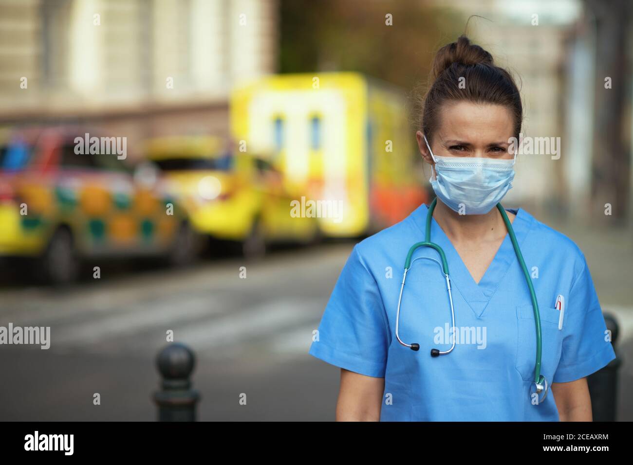 coronavirus pandemic. Portrait of modern paramedic woman in uniform with stethoscope and medical mask outside near ambulance. Stock Photo