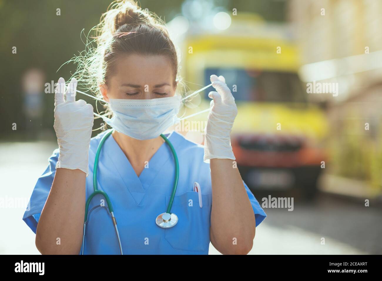 coronavirus pandemic. modern paramedic woman in scrubs with stethoscope and medical mask outside near ambulance. Stock Photo