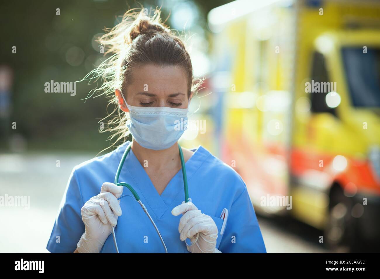 covid-19 pandemic. modern paramedic woman in uniform with stethoscope and medical mask outdoors near ambulance. Stock Photo