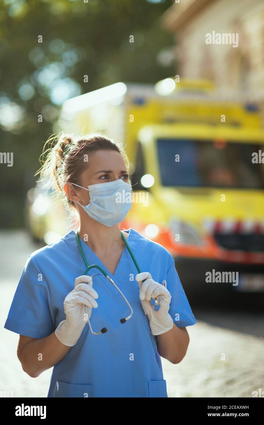 coronavirus pandemic. modern medical doctor woman in scrubs with stethoscope and medical mask outside near ambulance. Stock Photo