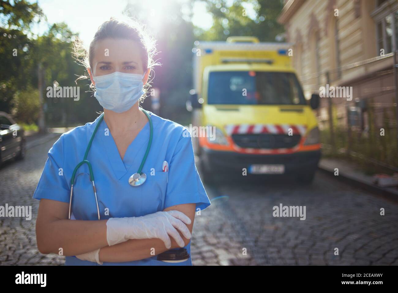 covid-19 pandemic. Portrait of modern paramedic woman in uniform with stethoscope and medical mask outside near ambulance. Stock Photo