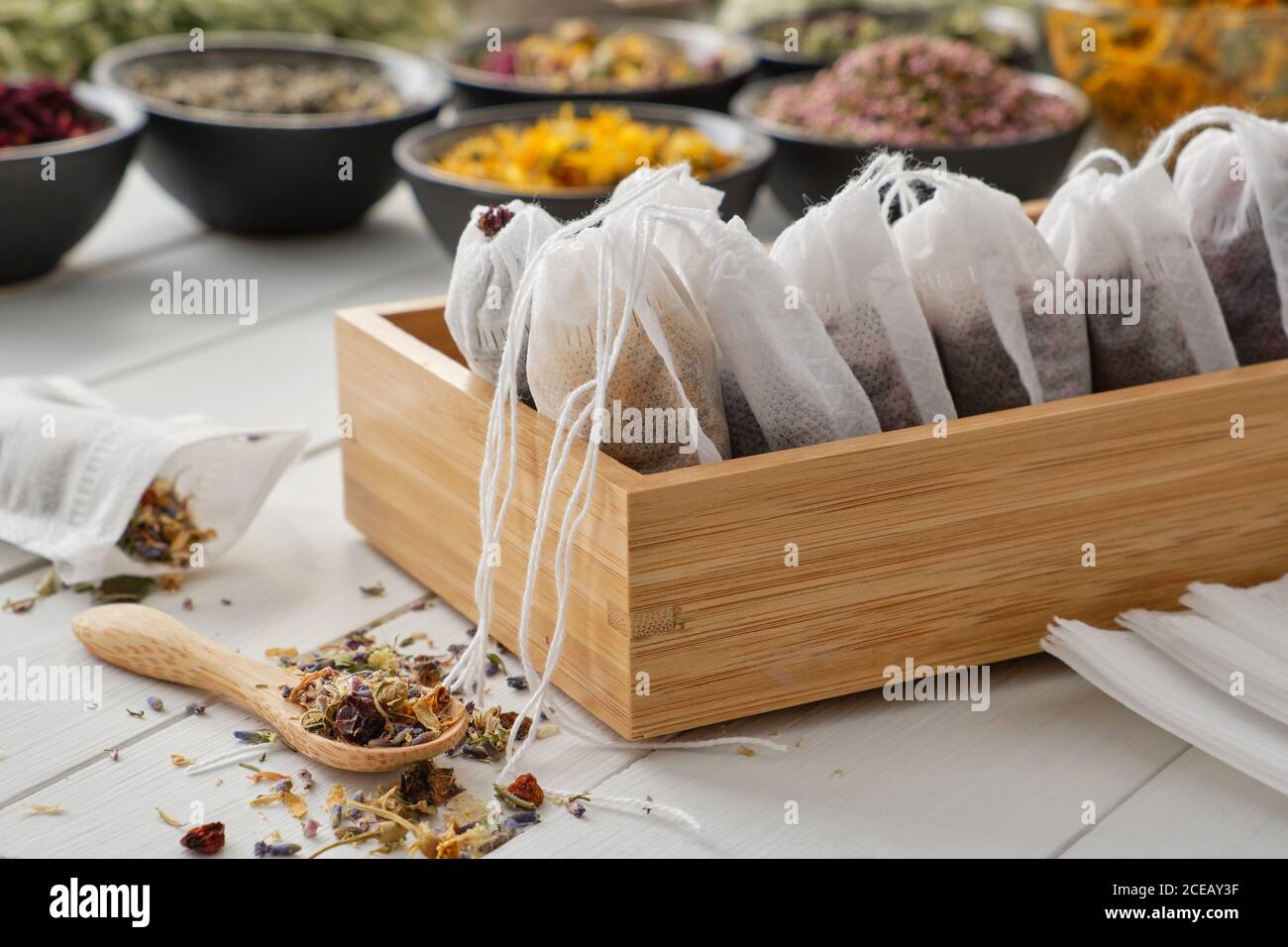 Wooden box of tea bags filled with dry medicinal herbs and flowers. Bowls of medicinal plants on background. Alternative medicine Stock Photo