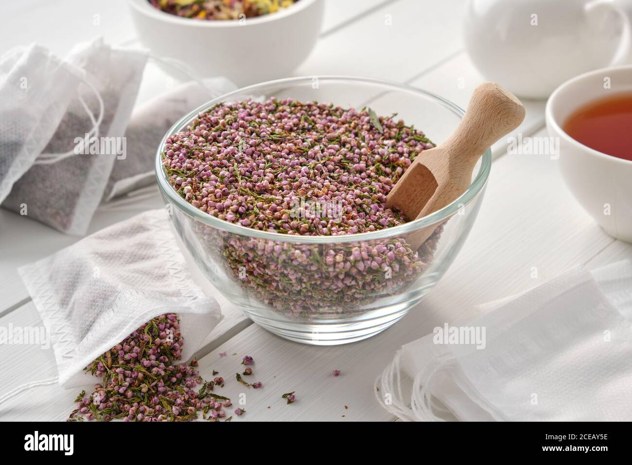 Bowl of dry healthy heather, tea bags with Еrica flowers. Herbal tea cup, teapot and mortar on wooden table. Alternative medicine. Stock Photo