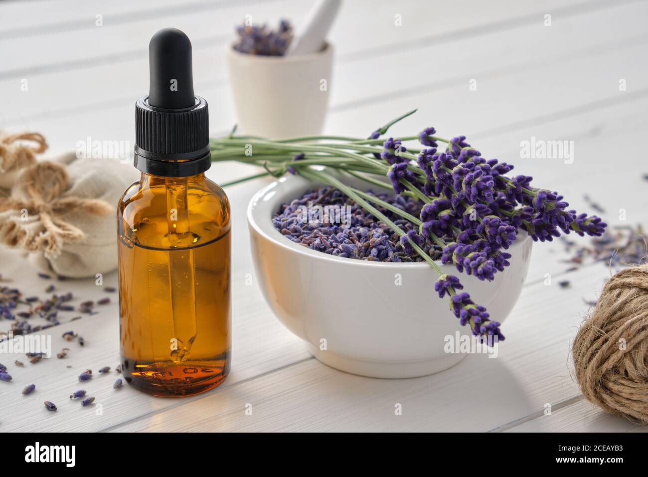 Dropper bottle of essential lavender oil, mortar of dry lavender flowers and sachets on white wooden table. Stock Photo